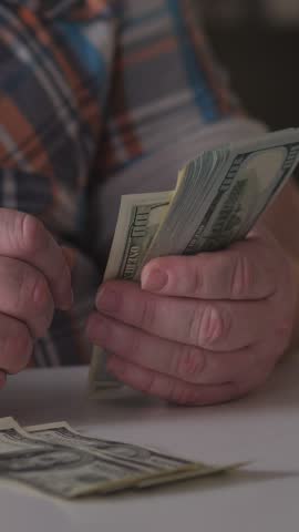 Man Counts Money Carefully, Person In Plaid Shirt Sorts Through Bills With Focused Lighting, Detailed View Of Man Counting One Hundred Dollar Bills On Table Under Bright Lighting