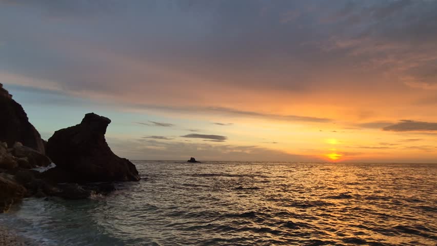 Sunset ocean coastline. Dramatic golden light reflects across choppy waves near rocky cliffs during dusk.
