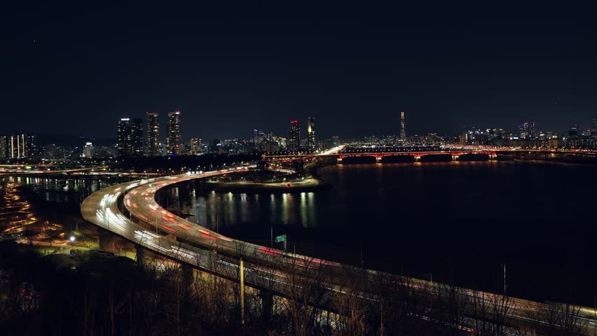 Dynamic high angle view of Seoul at night showing bustling traffic light trails on Seongsu Bridge and Gangbyeonbuk-ro highway with Lotte World Tower in background - timelapse