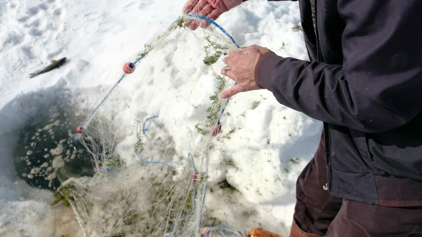 Fisherman setting a fishing net into an ice hole on a frozen lake in Kars, Turkey. Cinematic winter scene showing traditional ice fishing, rural life, cold weather and outdoor lifestyle concept.