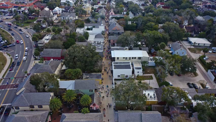 St Augustine in Florida features a historic street lined with buildings and trees, busy with pedestrians, and overlooking nearby waterfront docks, bridges, and harbor areas.