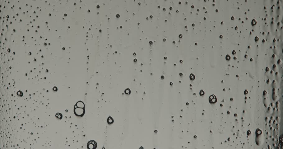 White soap foam flows down a transparent glass surface in low light, forming textured abstract vertical stripes. Slow motion.