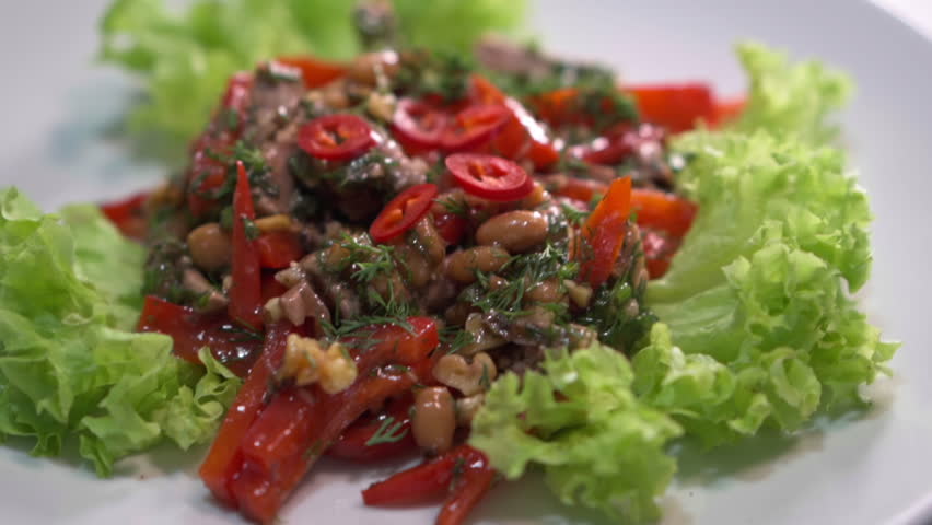 Appetizing warm salad with meat, red beans, bell peppers, walnuts, and chili peppers served on a bed of crisp lettuce leaves