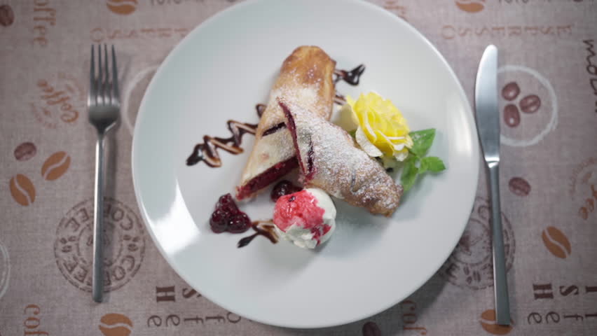 Sweet cherry strudel with vanilla ice cream, berry sauce and a delicate butter rose on a white plate. Fresh pastry ready to eat