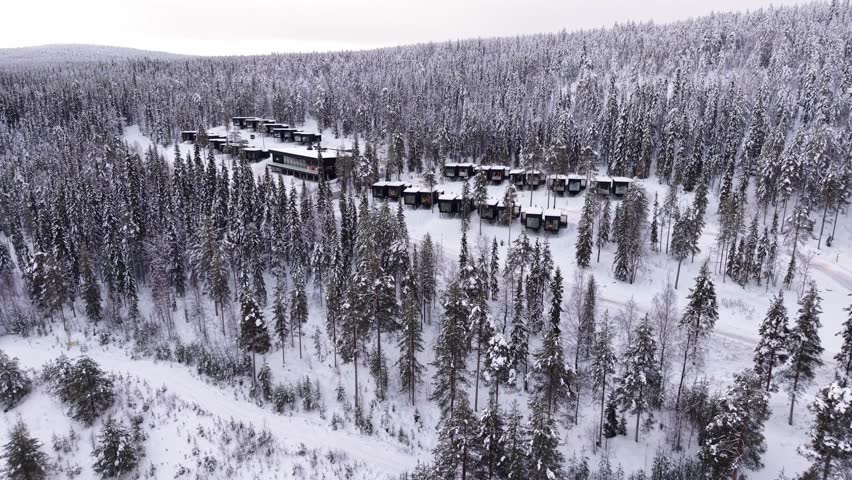 Aerial of winter holiday resort, glass cabins surrounded by pine forest covered in snow, Santa village, Lapland