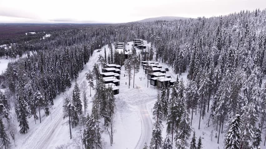 Winter resort surrounded by pine forest covered in snow, Glass cabins, chalets near Santa Claus village, Lapland, drone shot