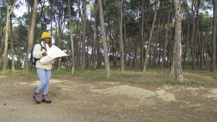 Young african american woman with a backpack consulting a map while walking on a forest trail