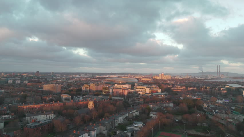 Dusk drone flyover from Herbert Park towards Aviva Stadium in Dublin, Ireland 4K drone footage at dusk flying over Herbert Park in Ballsbridge, Dublin, Ireland towards the illuminated Aviva Stadium, showing the rugby and football arena, city skyline, suburban streets and soft evening light.