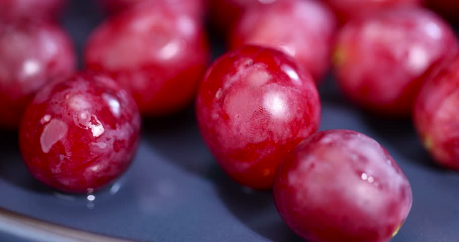 torn red grapes in drops of water on a blue plate , wet ripe and delicious red grapes on a plate on a black slate board