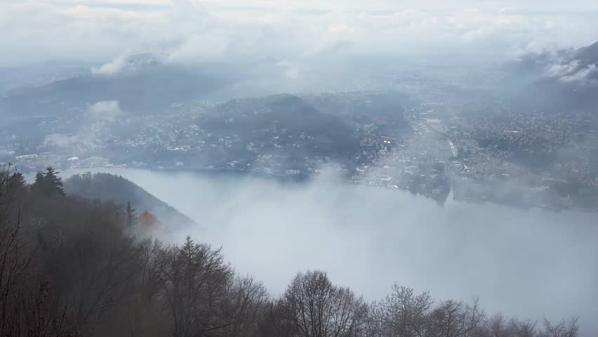 Morning fog at Como, Italy. Clouds over the Alps mountains and Como lake. View from Brunate mountain. Clouds moving over the mountains. Autumn landscape at cloudy day

