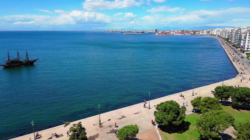 view of a vibrant Greek seaside promenade with people walking along the waterfront on a sunny day.
