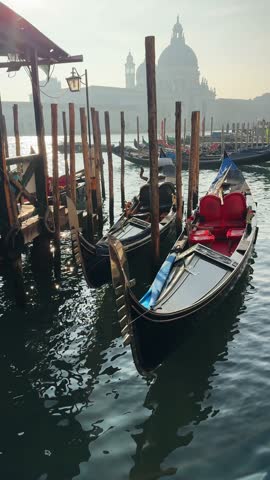 Gondolas moored on Grand canal near San Marco square in Venice, Italy. Basilica Santa Maria della Salute in the background. Beautiful cityscape at sunset. Vertical video
