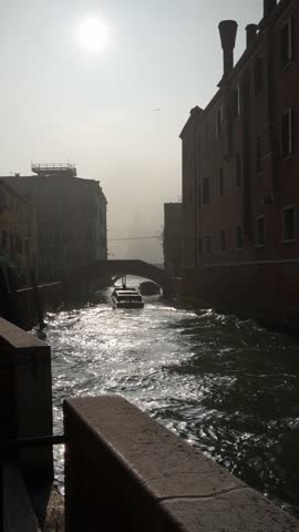 Old venetian architecture on the canal with bridge in Venice, Italy. Boats on the canal. Beautiful autumn cityscape at foggy sunrise. Famous travel destination. Vertical video
