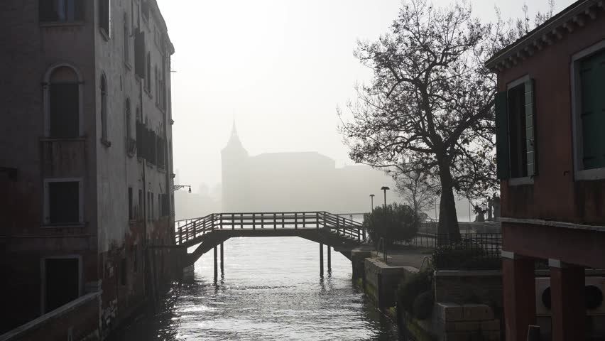 Foggy morning in Venice, Italy. Old venetian architecture and bridge on the canal. Grand Canal in the background. Beautiful winter cityscape. Famous travel destination
