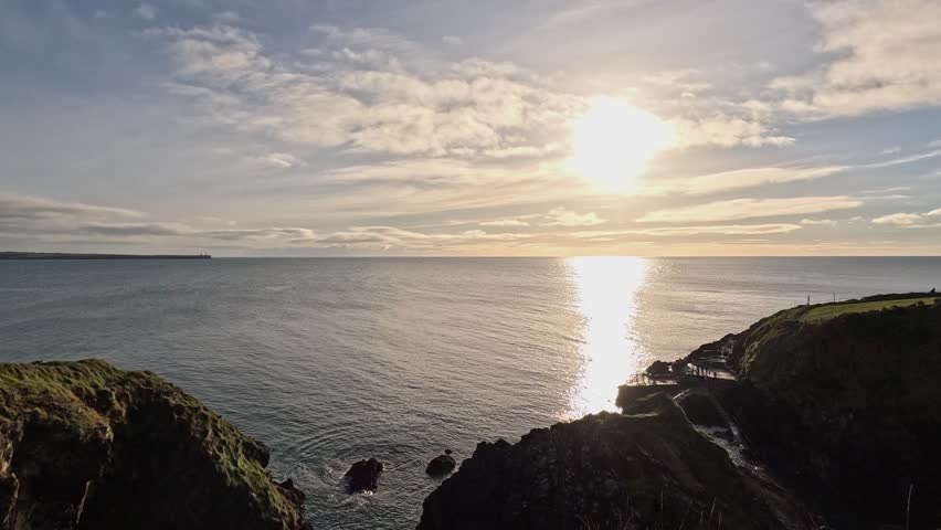 Golden afternoon sun leaves bright beam on calm ocean from cliff top