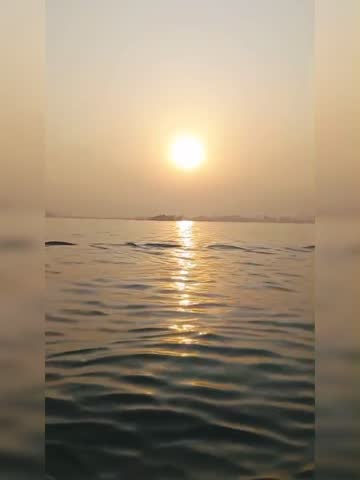 A serene sunset over a calm sea, with the sun casting golden reflections on the water's surface. The horizon is visible in the background, giving a peaceful and tranquil vibe perfect for nature or tra