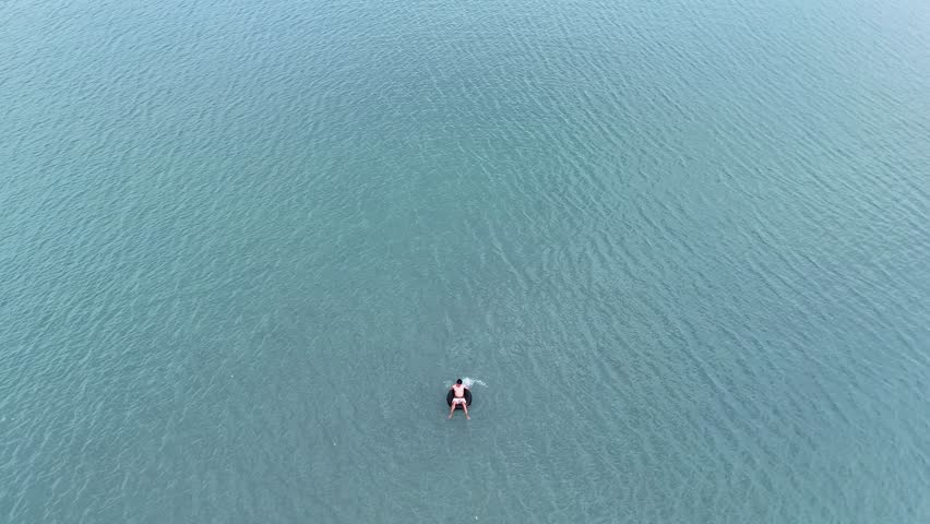 Aerial view of a person floating on an inner tube on a calm beach with gentle ripples.