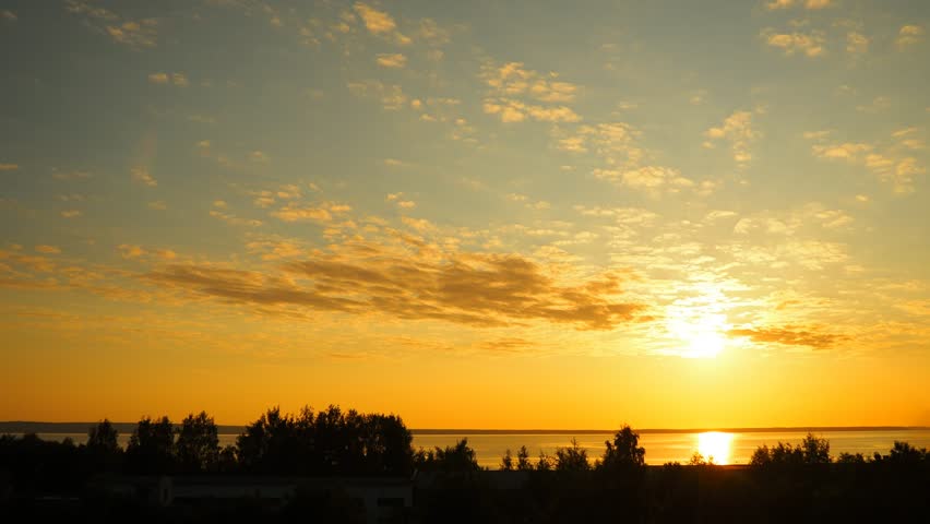 Sun rises over Lake Onega, casting a golden glow on tranquil waters. The horizon bursts with colors as mist dances above the surface, offering a serene and enchanting start to the day.