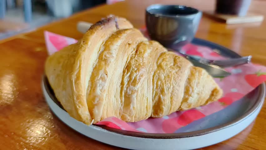 A close-up shot of a delicious croissant with a cup of coffee and utensils on a plate