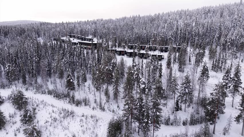 Winter resort glass cabins surrounded by pine forest covered in snow, Santa Claus village, Lapland, drone shot
