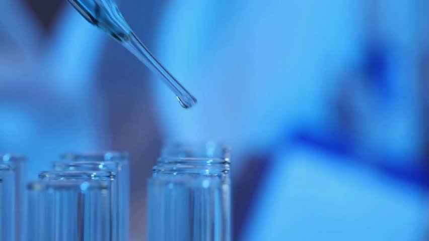 Pipette drips blue chemicals into a test tube. Closeup.