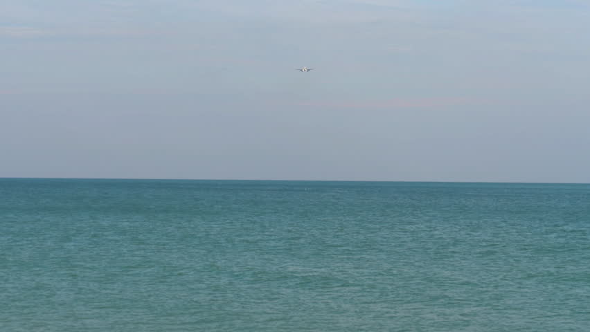 Jet commercial airplane approaching landing over azure sea, front view