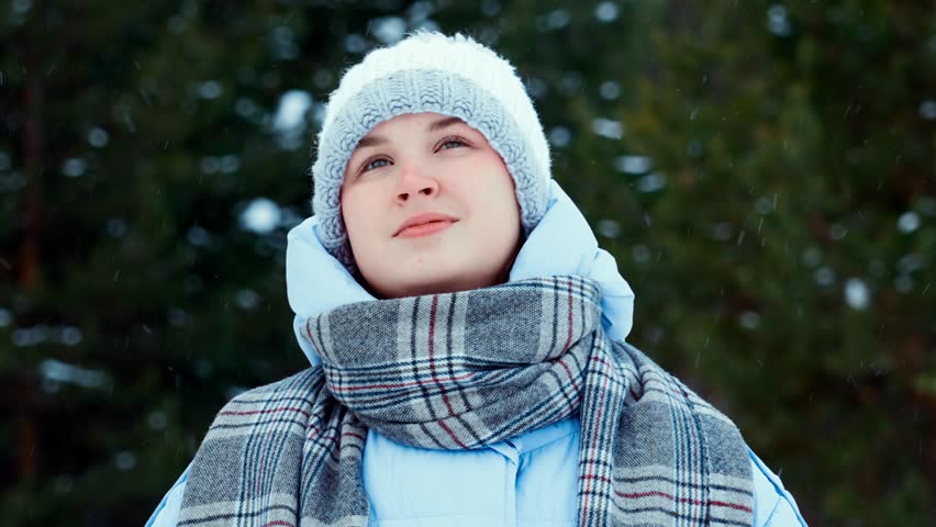 Portrait of a young girl enjoying winter and falling snowflakes in a snowy forest. People in winter.