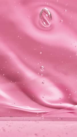 Transparent cosmetic liquid gel cream slowly drips flowing down on a pink background. Slime texture. Selective focus.