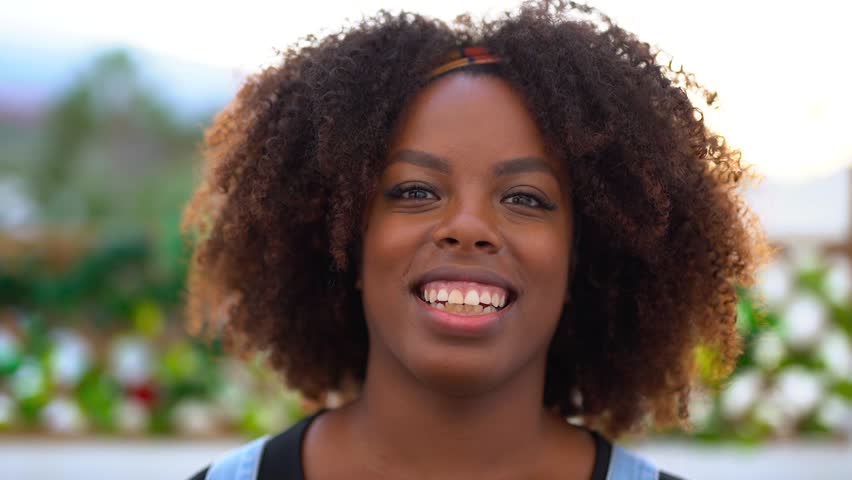 Happy young african woman with afro hair smiling in front of camera at house terrace - Lifestyle, trendy and cheerful people concept
