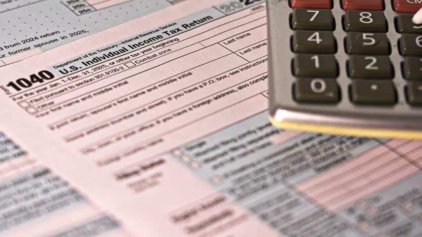 Accountant using a calculator to complete a 1040 tax form before the filing deadline