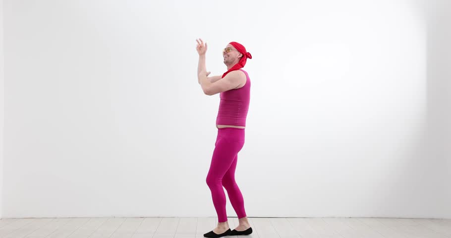 Funny man in pink costume dances in empty studio room. Energetic dancer waves arms while stepping forward with playful rhythmic groove slow motion