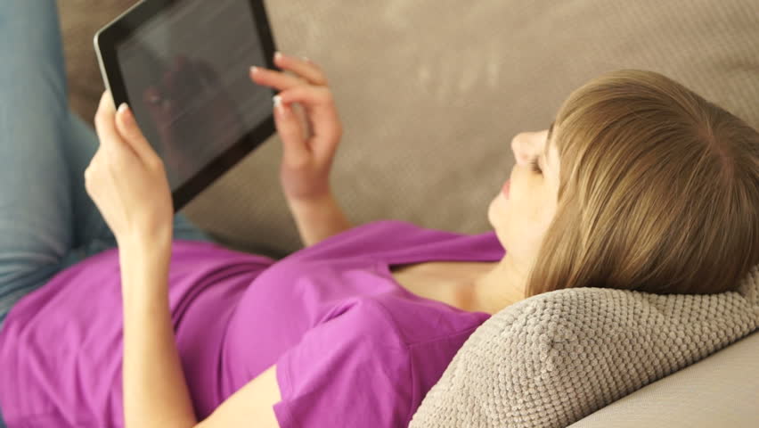 Woman resting on sofa with tablet pc and looking at camera with smile
