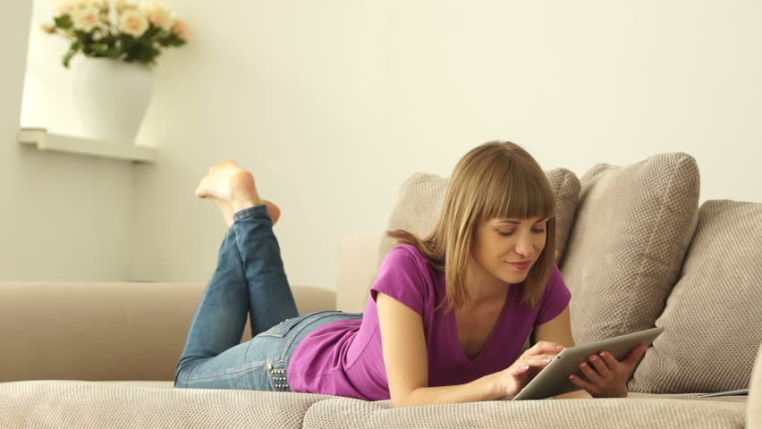 Young adult resting on sofa with tablet pc and smiling
