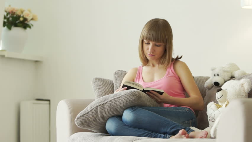 Young woman sitting in living room and reading book
