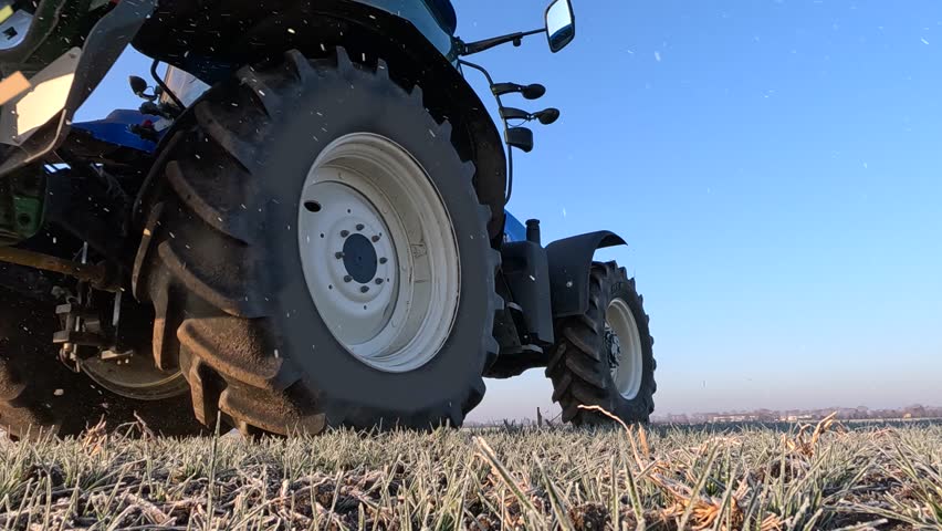 Farmer with agricultural machinery fertilizing wheat field in winter time, slow motion. Spreading mineral fertilizer, landscape rural scene - low angle shot