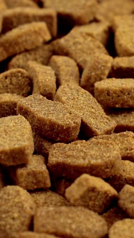 Brown kibble pieces of dry fish cat food circle rotation close up, vertical video format