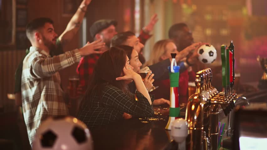 Group of excited, diverse friends cheering and celebrating a goal while watching a soccer game in a crowded and lively sports bar together