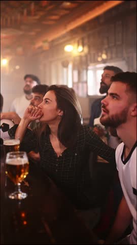 Young friends anxiously watching a soccer match at a crowded pub. Tense supporters cheering and celebrating victory, toasting with beer