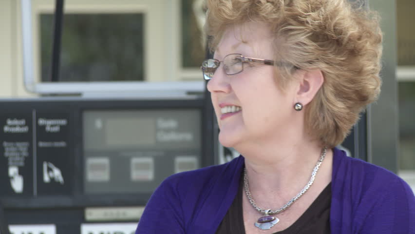 Close up on a happy, relaxed woman with gas pump and service station in the