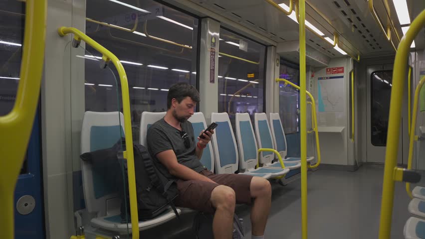 Traveler waits in modern Metro do Porto train using internet on smartphone. Empty carriage highlights comfort of public transport linking city center with airport stations