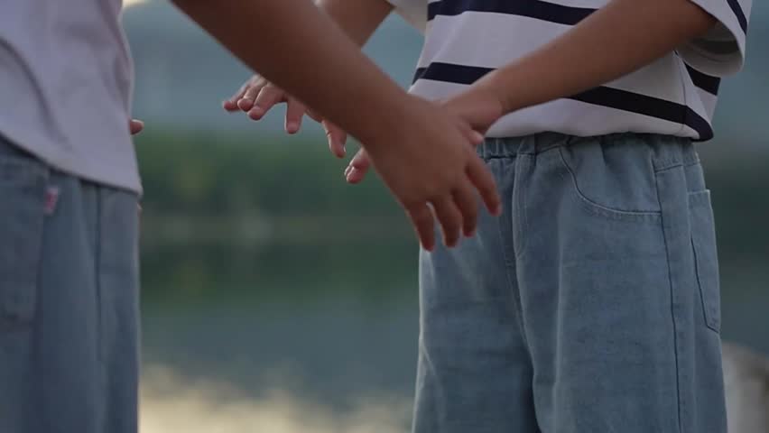 Two Asian siblings holding hands and praying together with eyes closed in morning light.