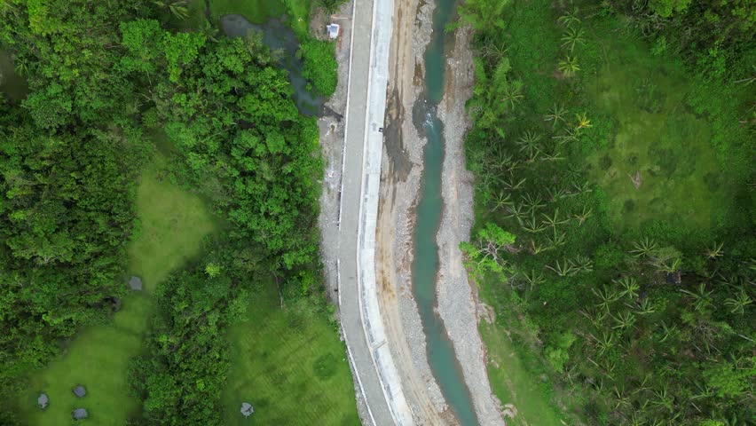Aerial top-down view of a scenic, concrete promenade along a shallow river and vibrant, dense tropical greenery - Philippines
