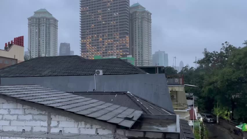 Urban cityscape with residential rooftops in the foreground and modern high-rise buildings in the background during a rainy morning. City neighborhood with tall buildings, overcast sky, and urban development.”