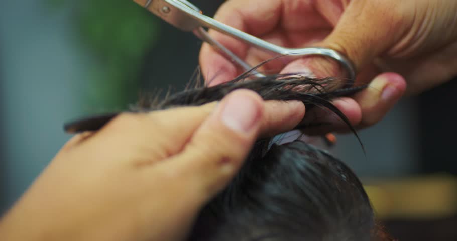Macro detail of scissors cutting hair strands with gloved hands in a barber shop, grooming and beauty service concept.