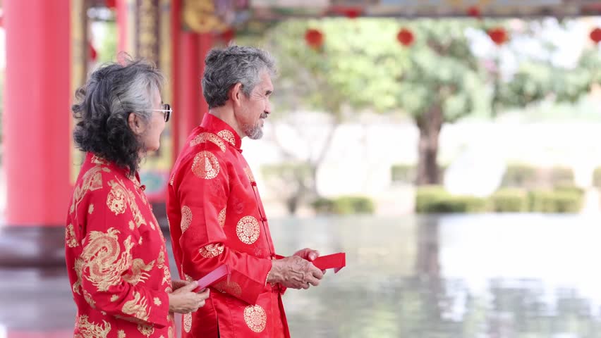 Asian family with senior parent in red cheongsam qipao dress is exchanging fortune tangerine and red envelope at Chinese Buddhist temple during lunar new year for best wish blessing and good luck