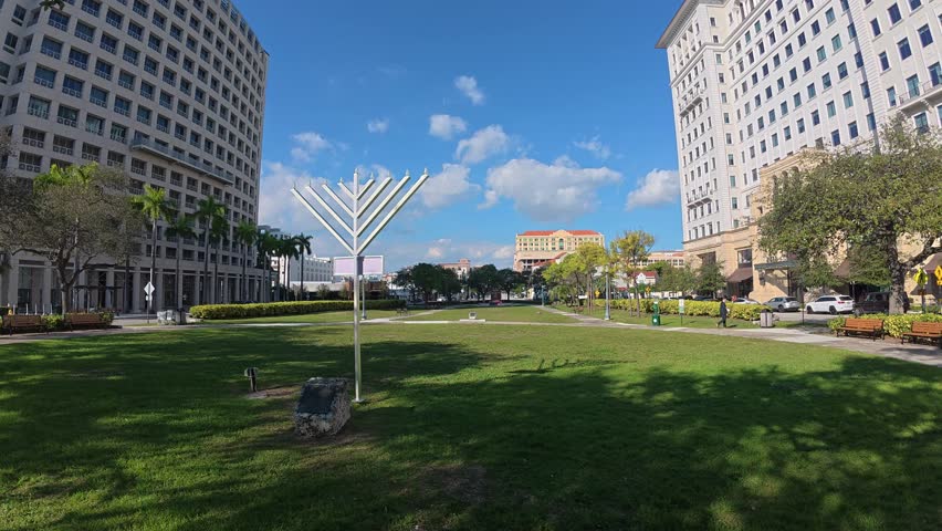 A wide angle view capturing an expansive grassy lawn within a city park environment.

