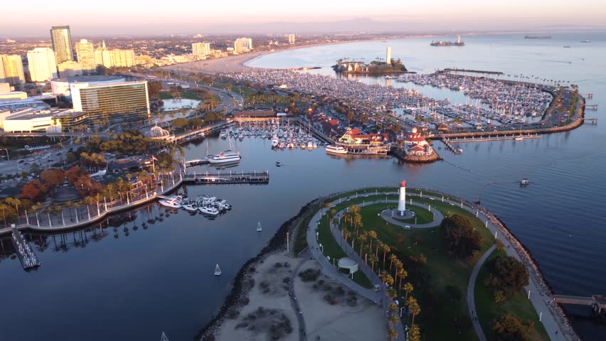 Establishing shot of Long Beach, California at Sunset showing the Queen Mary ship, harbor marina, waterfront walkways, docked boats, and calm waters of Queensway Bay over to Grissom Island.