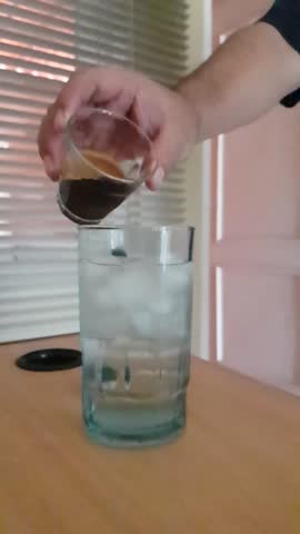 a small cup of espresso poured over cold water and ice cubes.