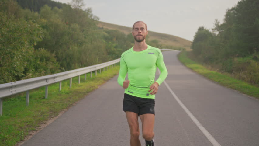 Runner trains outdoors, Individual engages in endurance running on isolated country highway at dawn amid cloudy weather