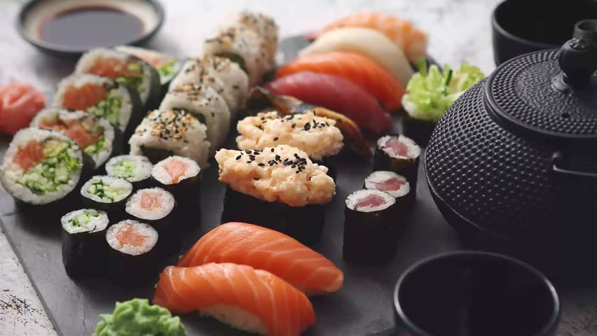 A beautifully arranged platter of fresh sushi and rolls, complete with wasabi, ginger, and a traditional teapot